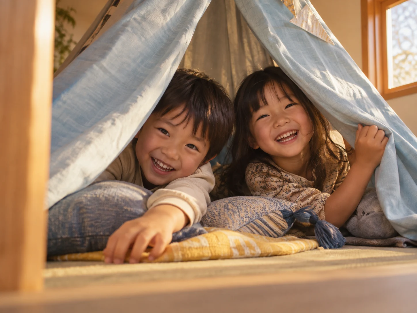 夕方の光の中、布の秘密基地で笑う二人の子どもに寄ったイメージ